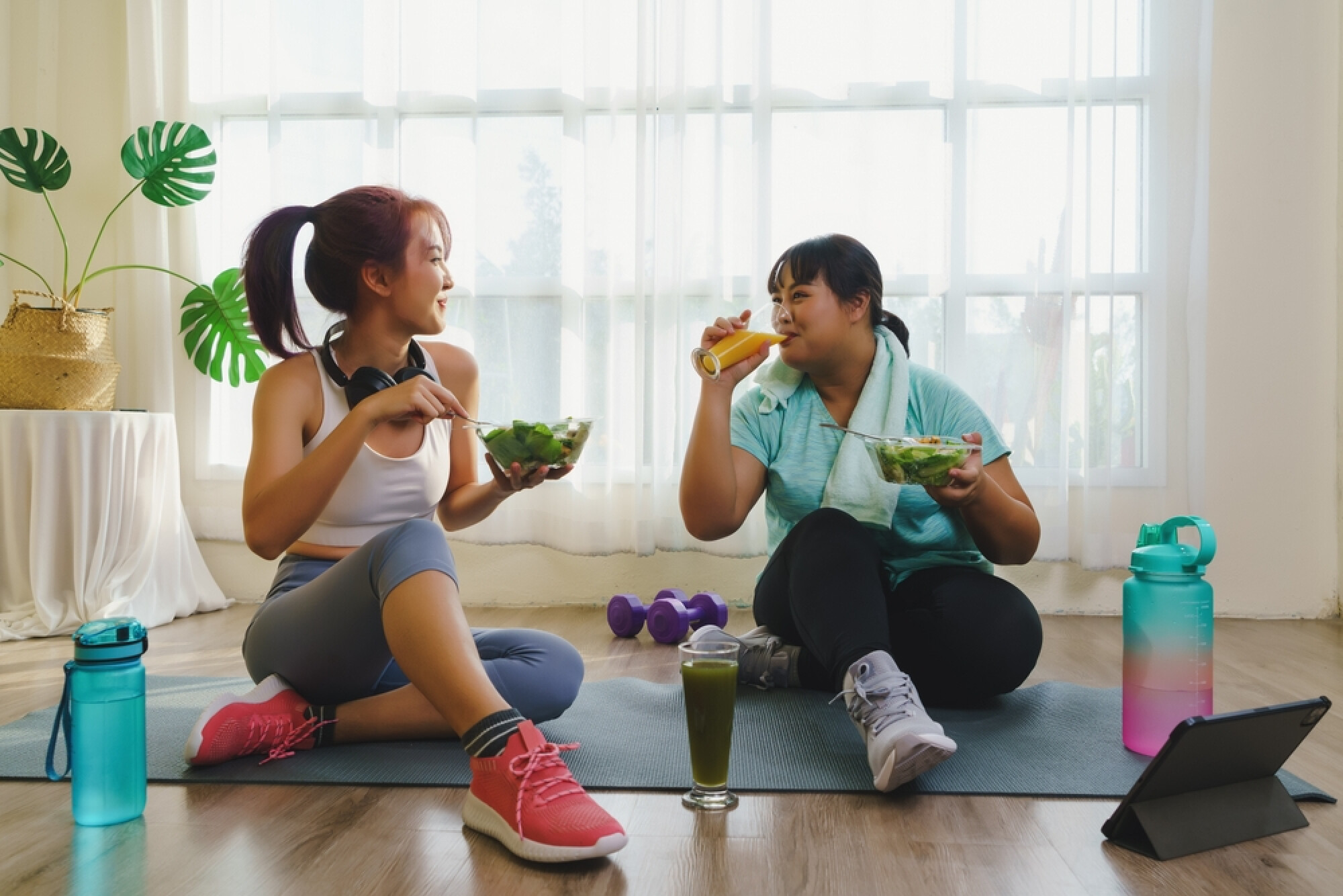 两位女士坐在瑜珈垫上一边饮食一边交谈，展现了运动后进食的轻松气氛