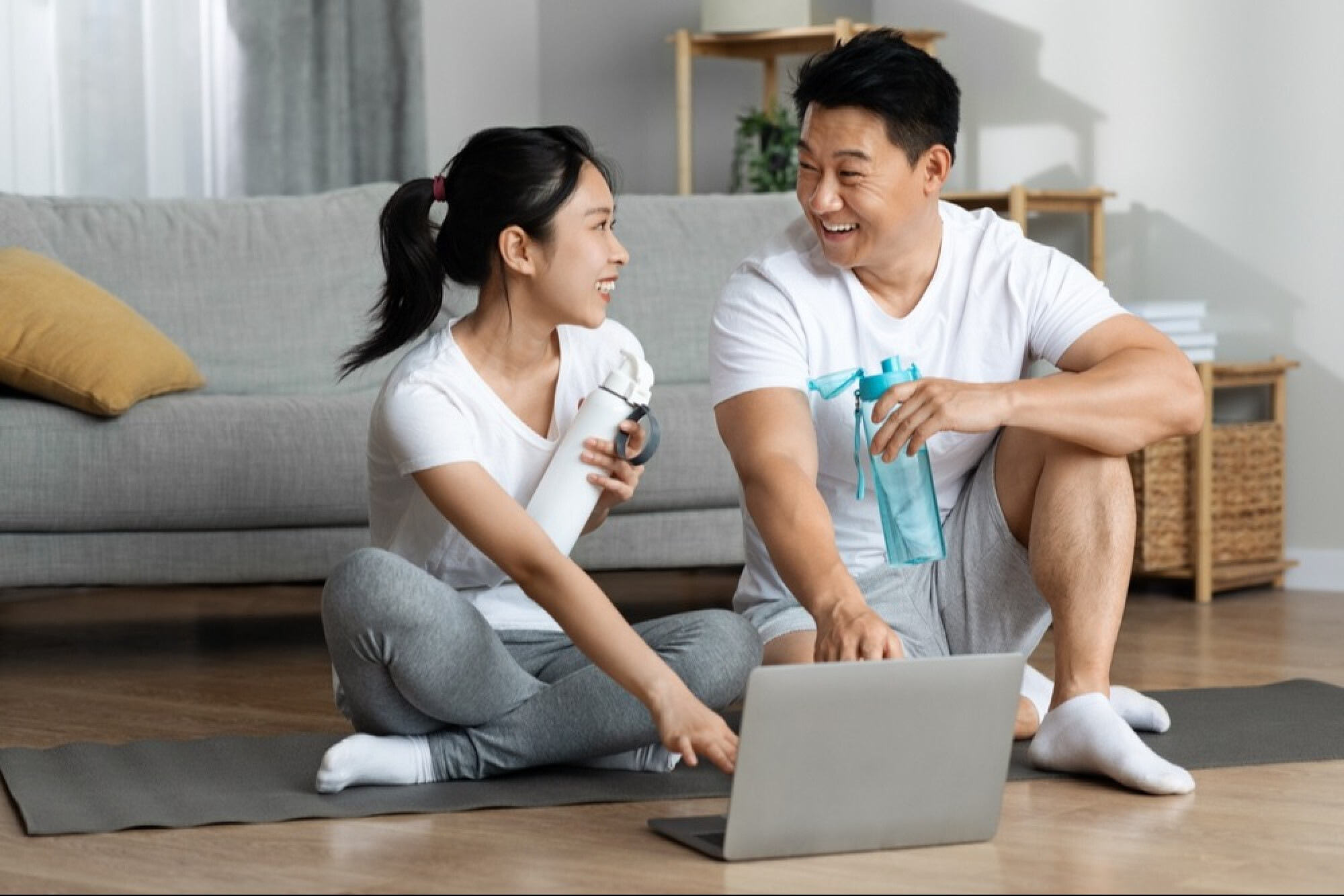  一对男女坐在瑜珈垫上，展示了运动后要适量补充水分。