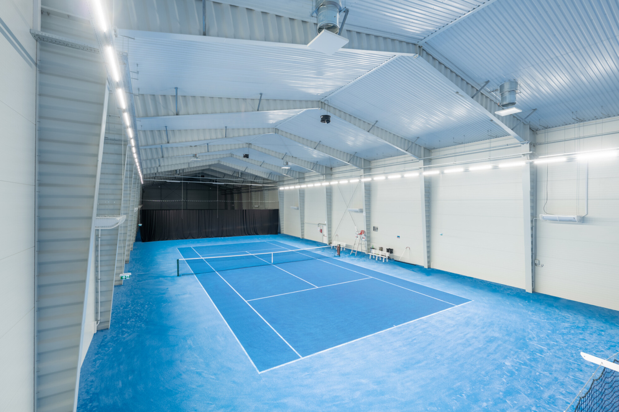 寬敞明亮的現代化專業室內網球場，舖設藍色硬地並配備完善照明系統，展示不受天氣影響的優質打球環境。
