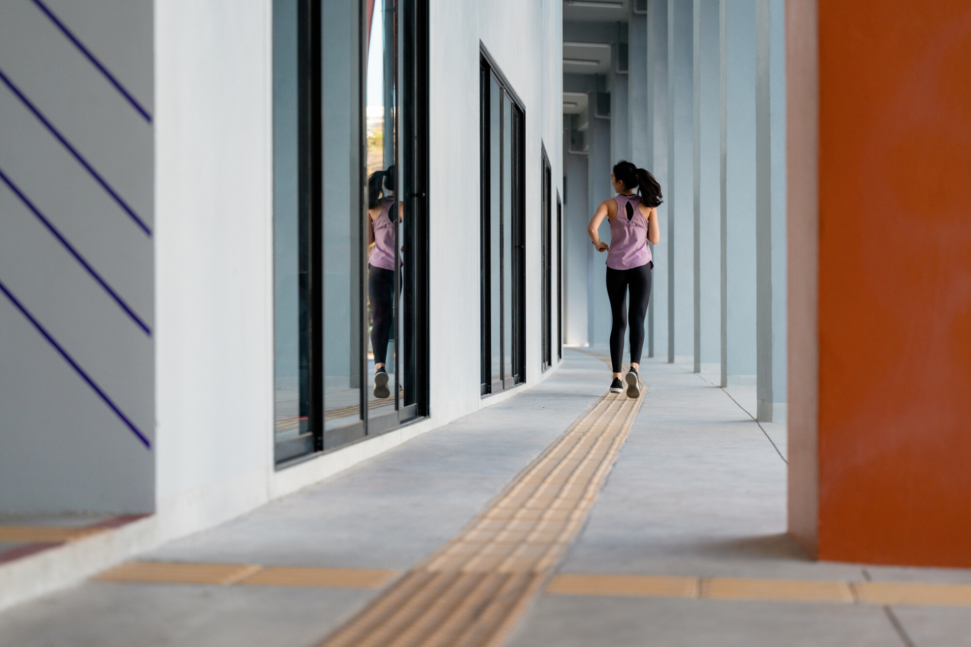 女子在設有觸覺引路帶的寬闊走廊上跑步，展示適合不同人士使用的無障礙室內跑步路線環境。