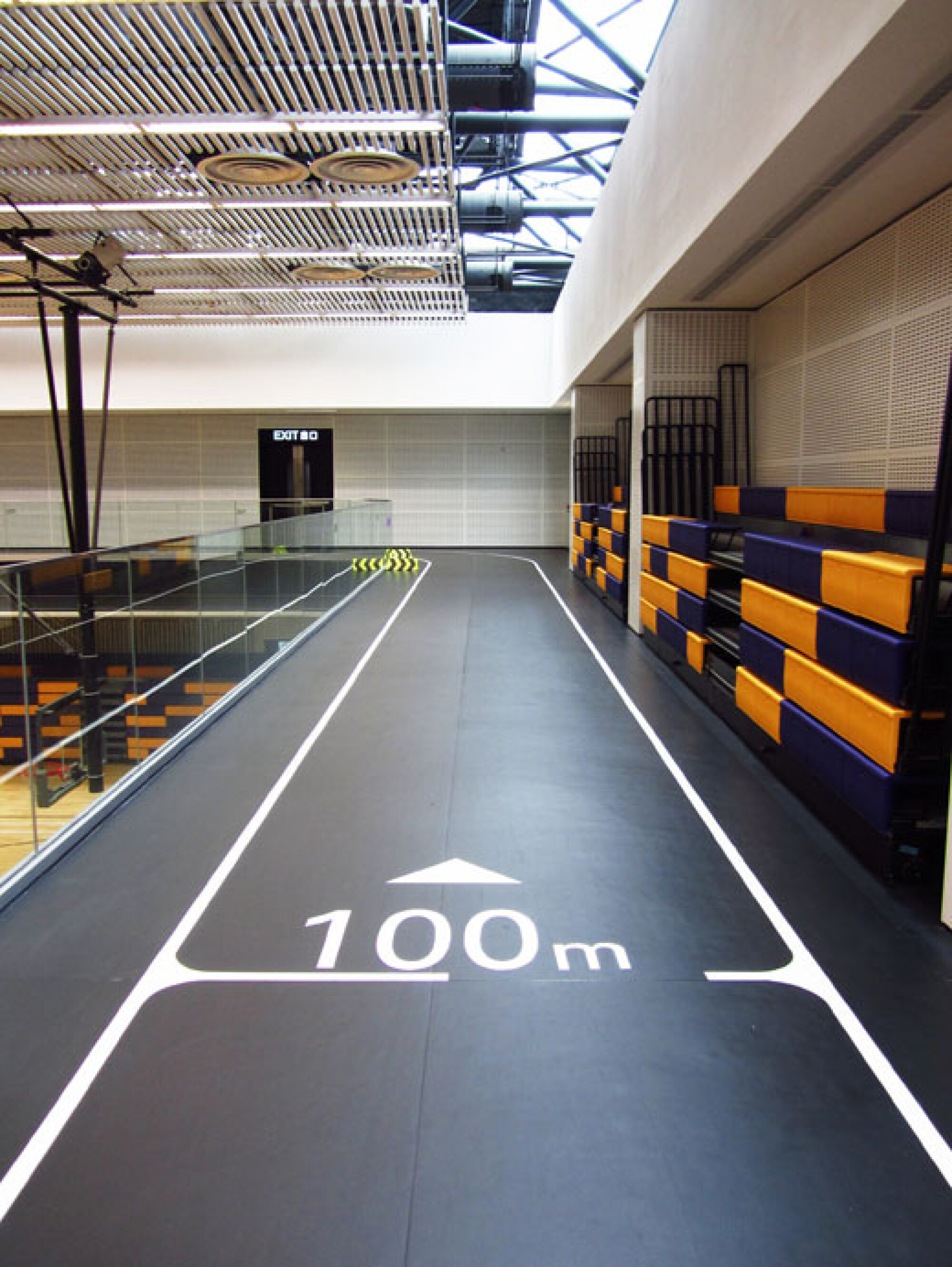 坑口體育館室內緩跑徑，黑色跑道上設有清晰的 100 米距離標記及方向指示，方便跑手計算訓練距離。