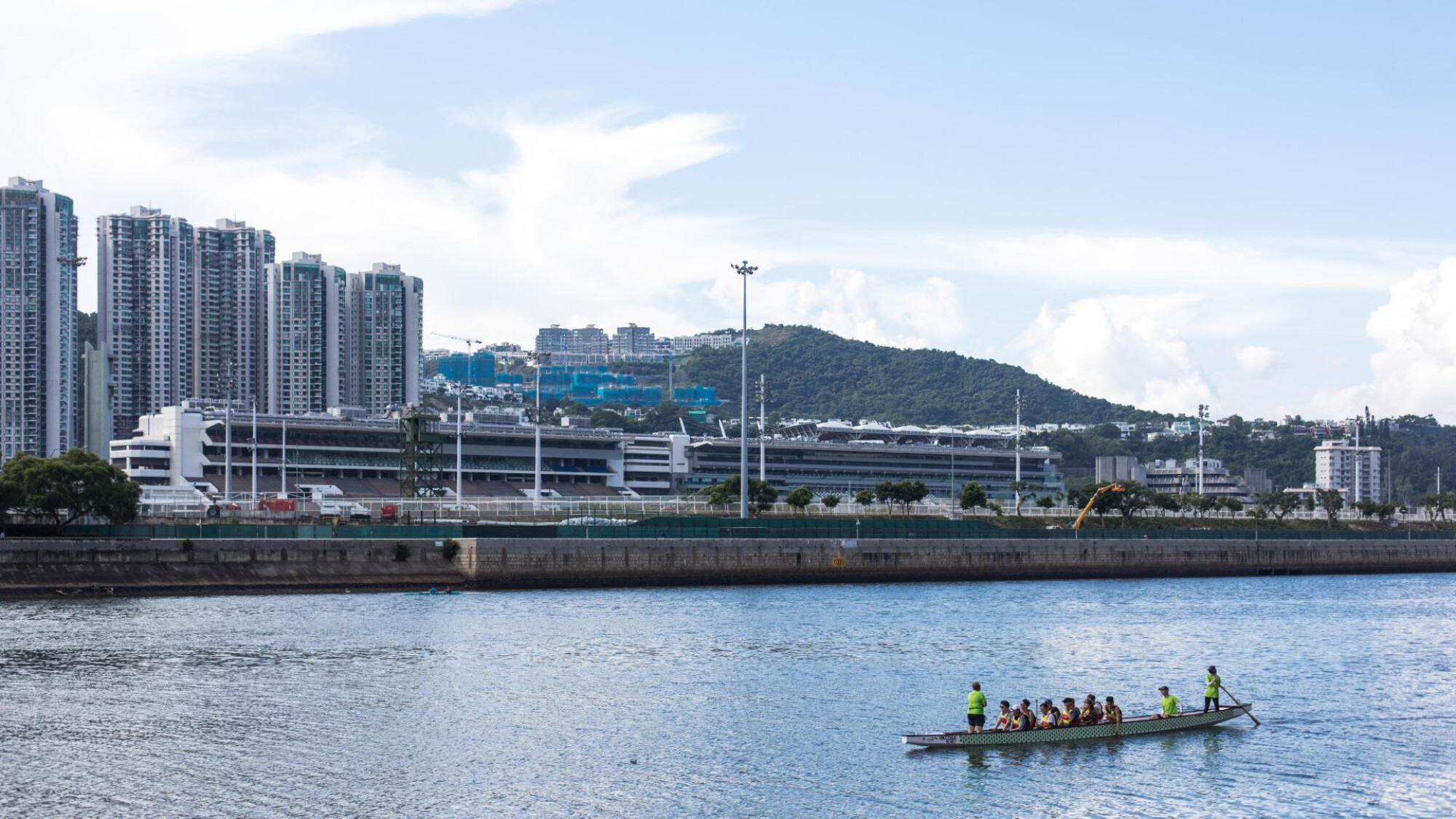 沙田城門河上龍舟隊伍正在進行划槳訓練，背景可見沙田馬場看台與高層住宅大樓，呈現香港城市水上運動風貌。