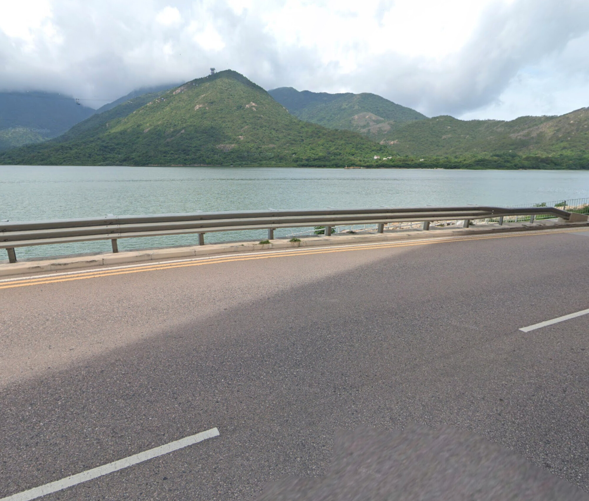 從道路護欄旁眺望翠綠青山的開闊景色，遠處可見纜車塔，展現適合戶外跑步或騎行的寧靜自然環境。