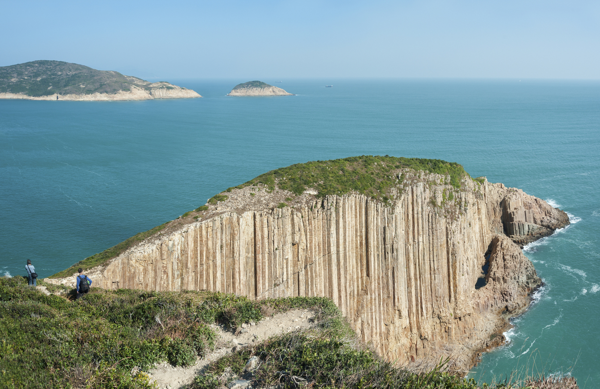 從高處俯瞰，一群行山客正沿著香港西貢的山徑健行，遠方是連綿的山脈和海景。