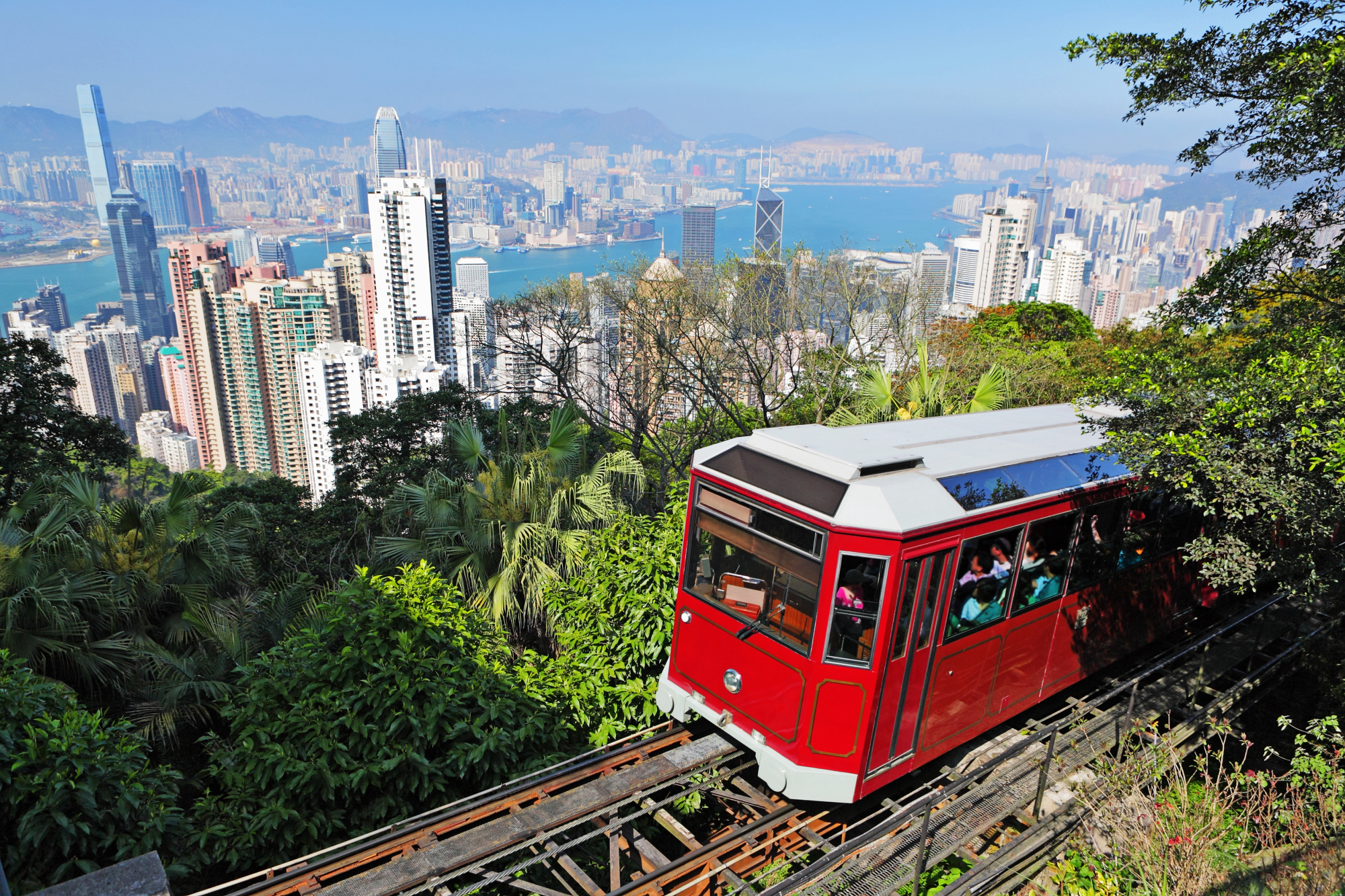 Image 3.jpg The red Peak Tram in Hong Kong is ascending the tracks, with a view of Victoria Harbour and the city skyline of Hong Kong Island and Kowloon in the background.