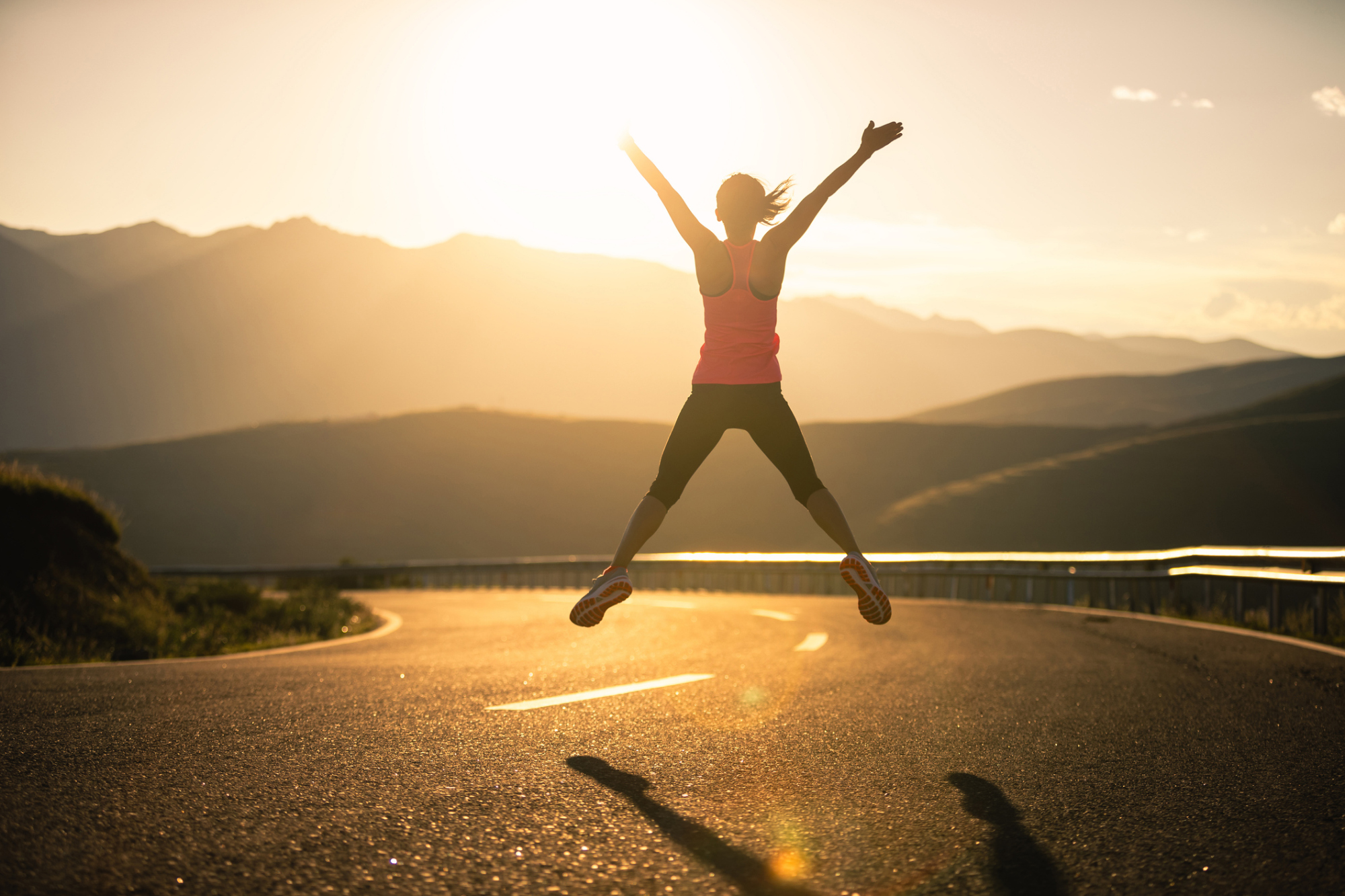 女子在日落時分的公路上進行跳躍熱身運動，藉此提升心率與體溫。