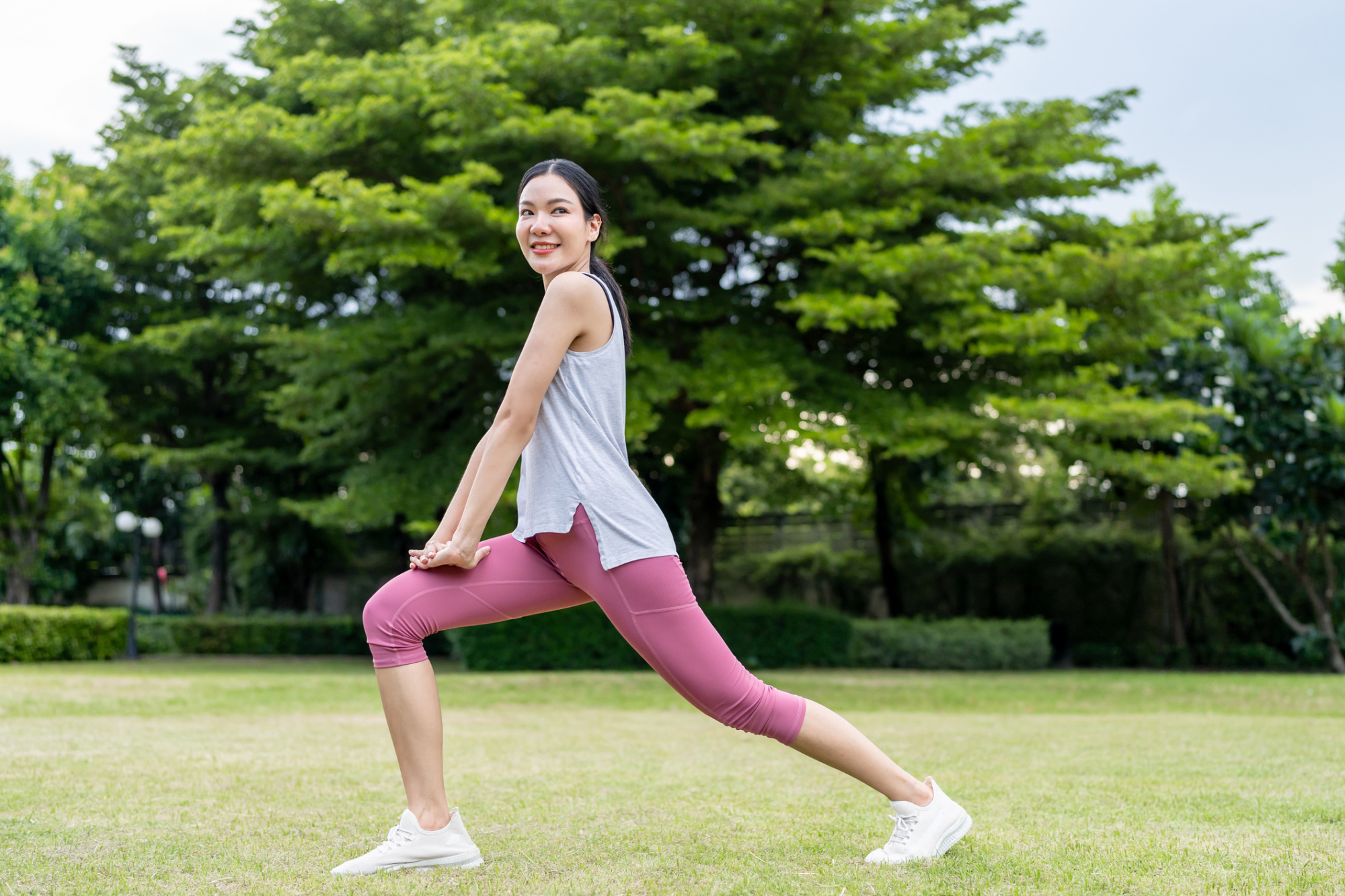 iStock-2178368968.jpg 女子在公園草地上進行弓箭步伸展熱身,跨步下蹲以伸展髖屈肌與大腿前側肌肉。